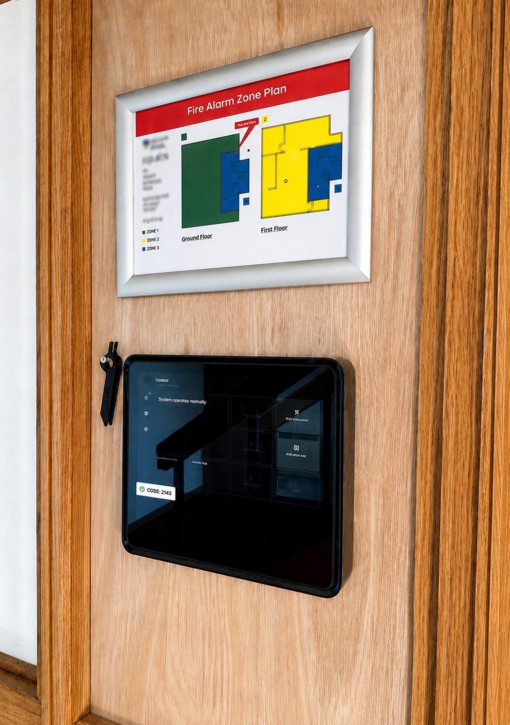 Ajax EN54 fire alarm control panel installed beside a fire alarm zone plan and manual call point